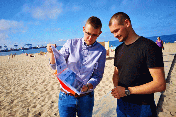 Two men are looking at a file of photos on a beach.