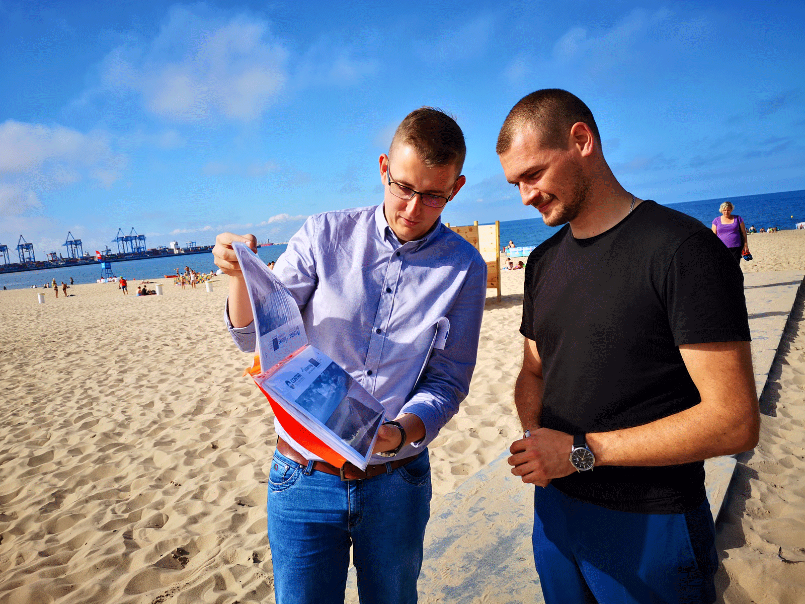 Two men are looking at a file of photos on a beach.